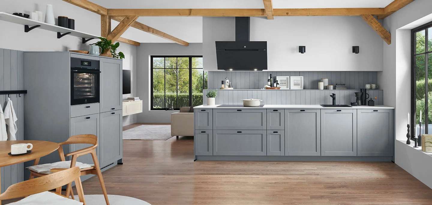 Moderne Landhausküche von nobilia mit grauen Fronten, Holzdecke mit sichtbaren Balken, großen Fenstern und offenem Übergang zum Wohnzimmer
