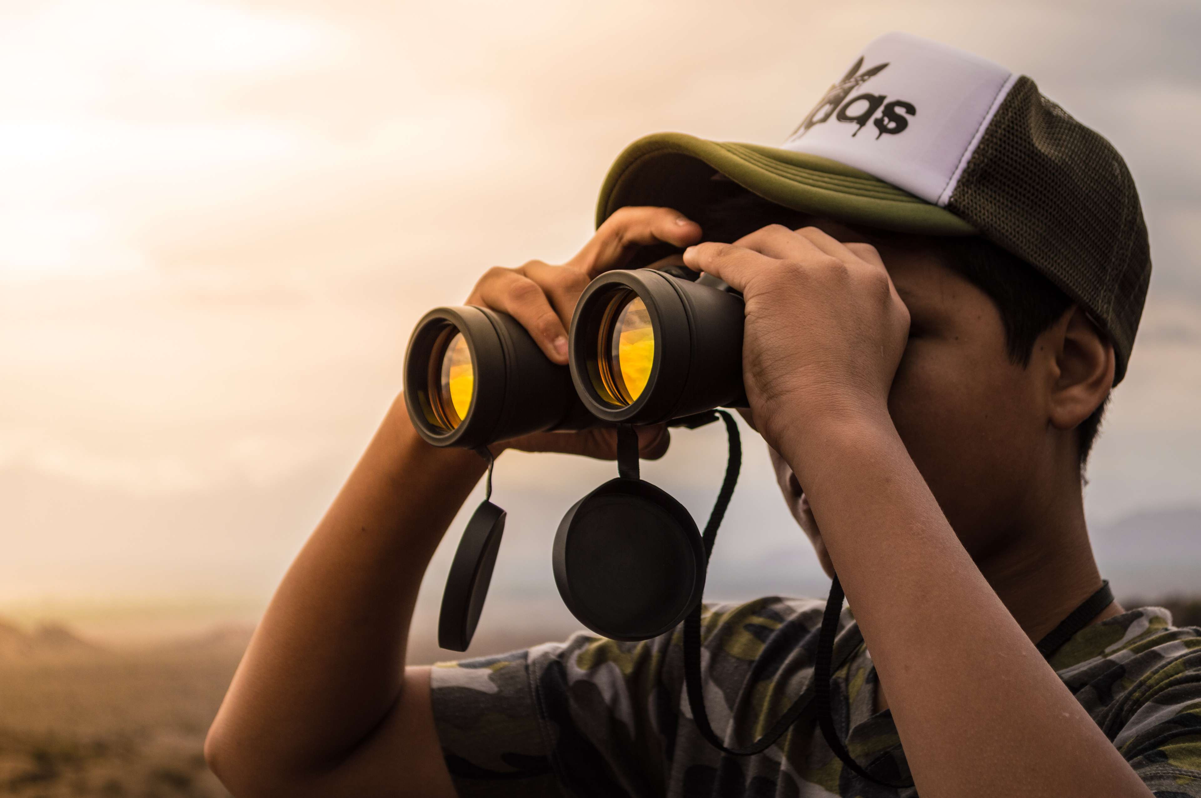 Junger Mann schaut während eines Sonnenunterganges durch ein Fernglas 