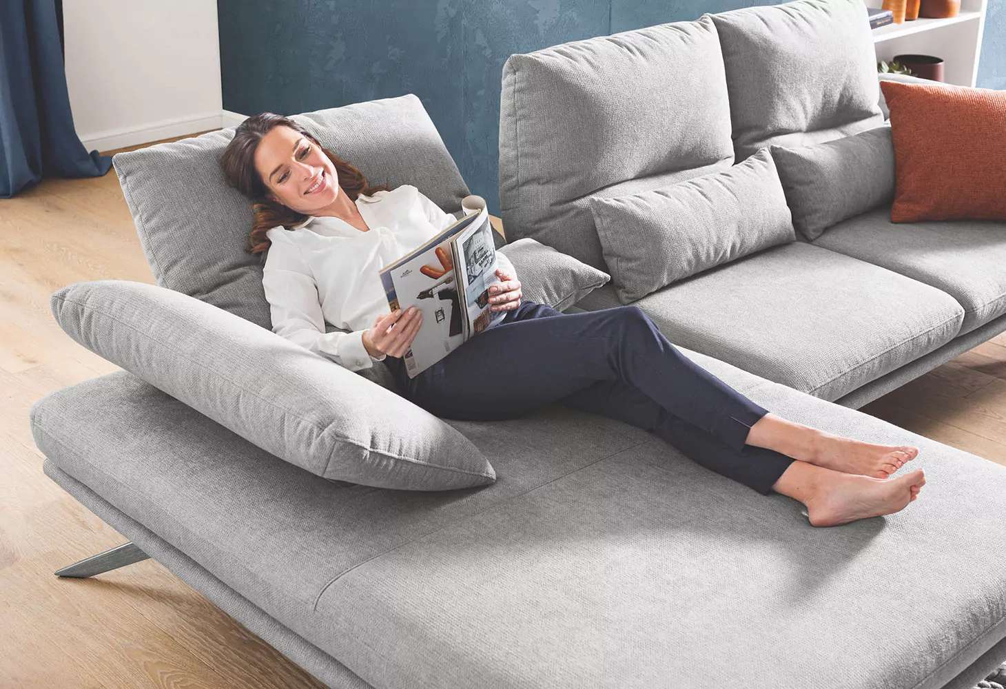 Junge Frau luigt auf einem Sofa und liest ein Magazin