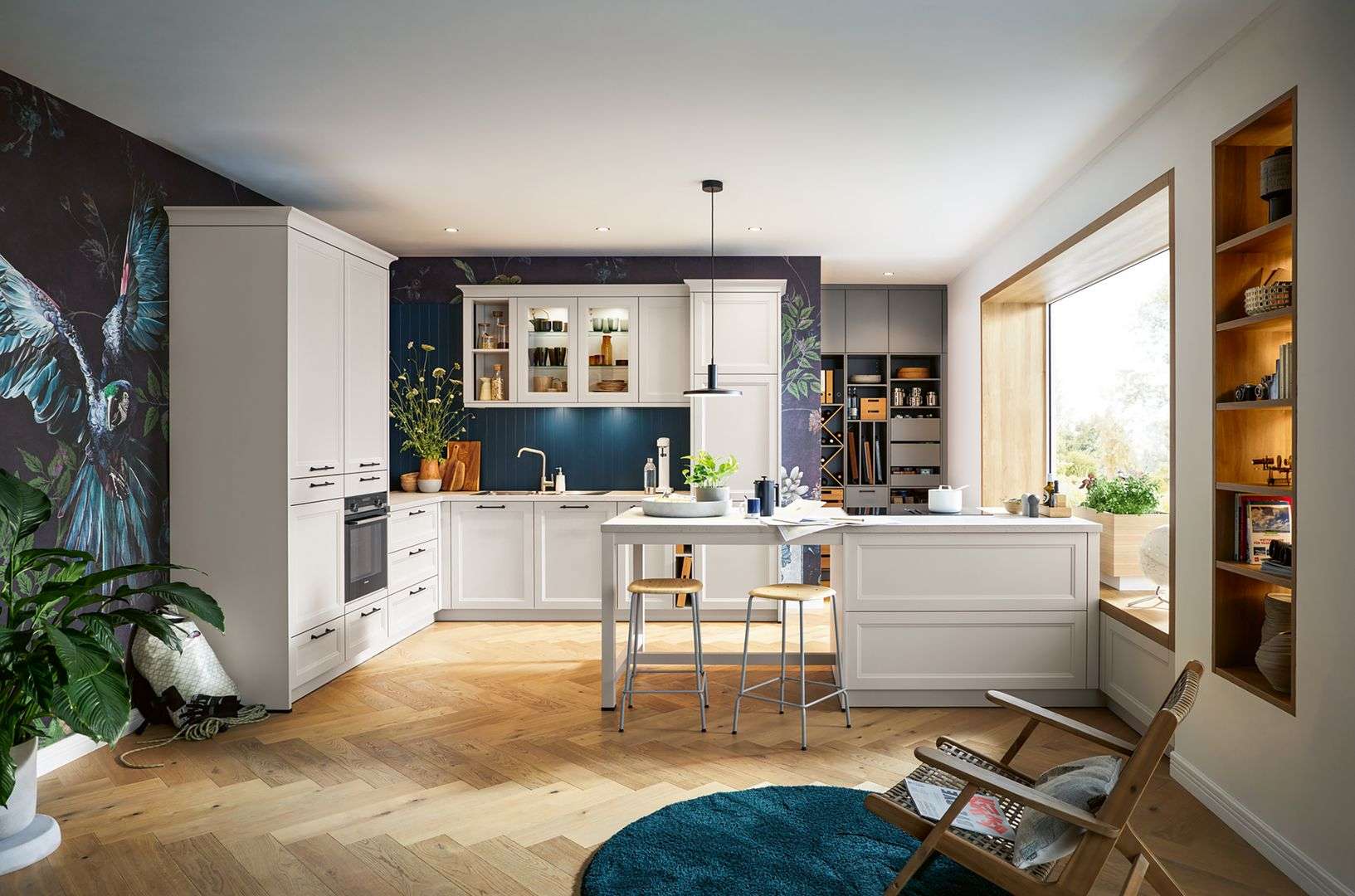 Landhausküche von Schüller mit weißen Fronten, Kücheninsel mit zwei Hockern, dunkler Wand mit floralem Muster und großem Fenster mit Sitzbank.
